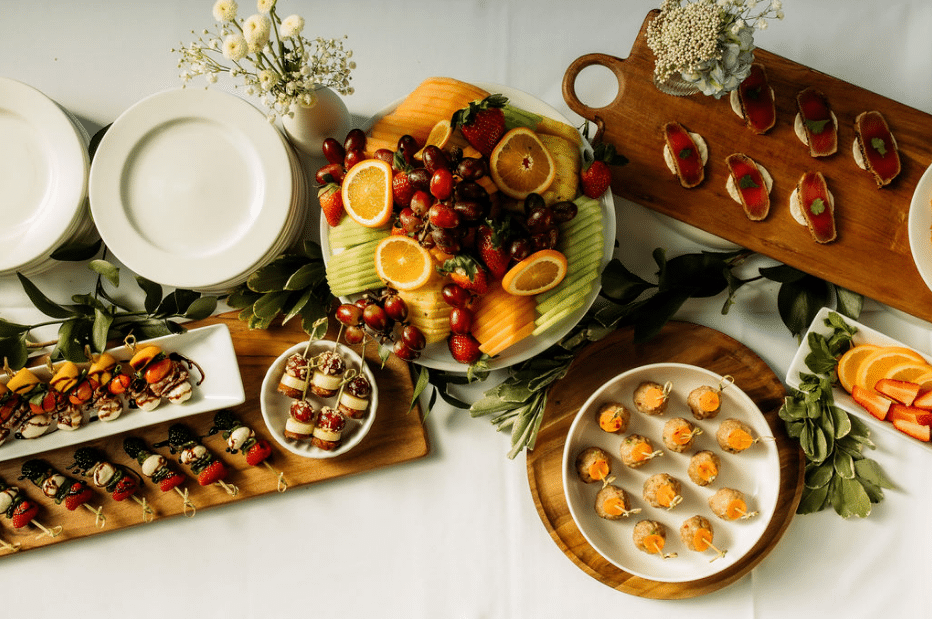 Gourmet catering display featuring fresh fruit platter, miniature appetizers, and crudités arranged for a formal event.