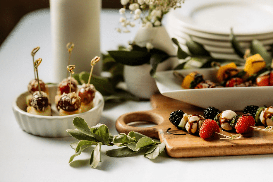 Close-up of elegant catered appetizers, including fruit and cheese skewers, arranged on wooden cutting boards for an event.